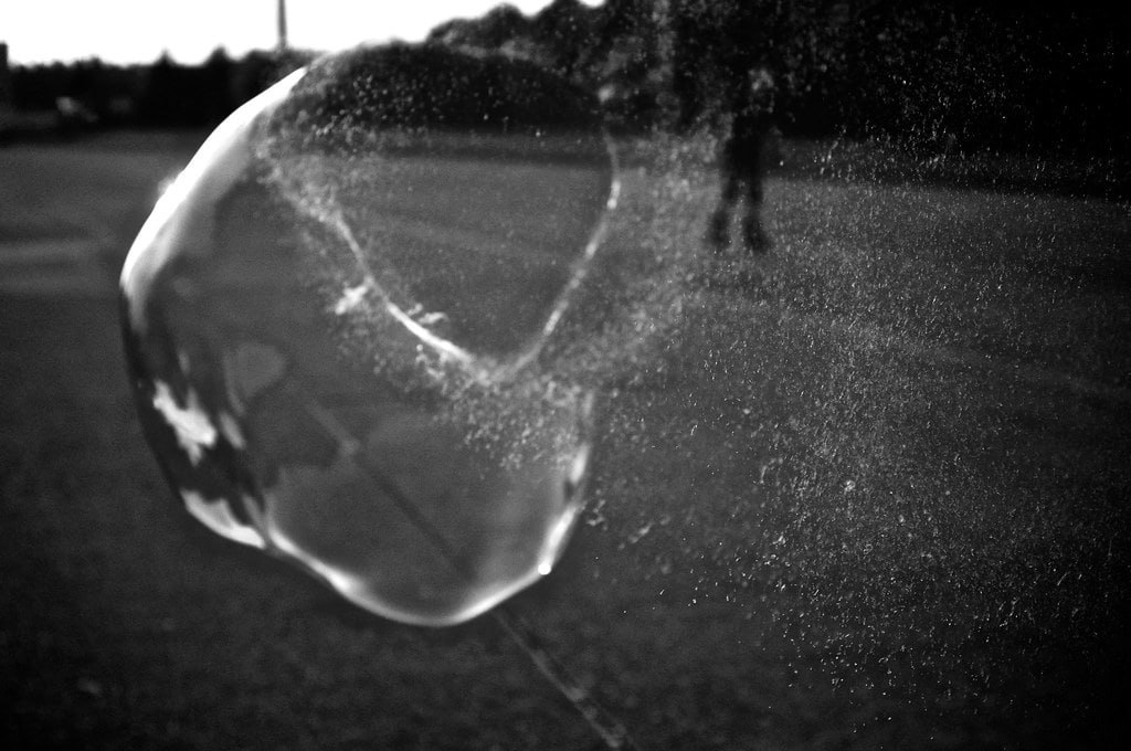 A bubble bursting while floating on the street. Picture in black and white