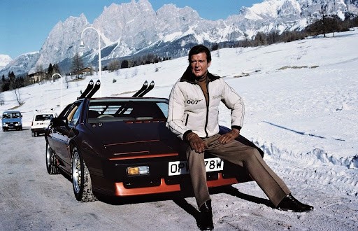 Roger Moore in the Alps sitting down on a red car during For your eyes only filming